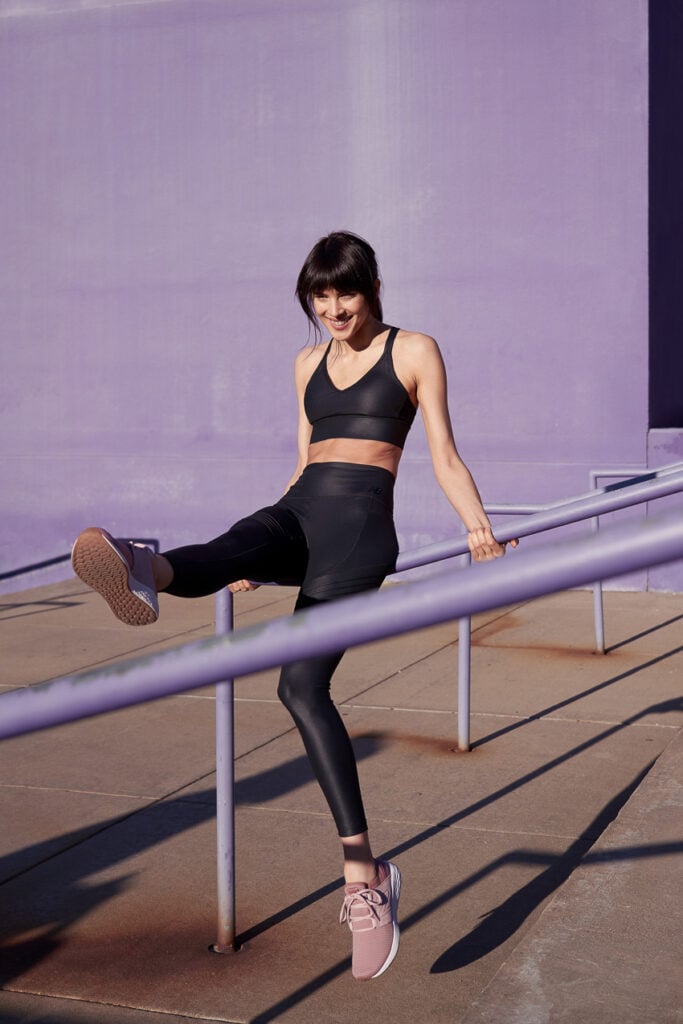 Photo of a woman sitting on a stairway's handrail while extending her leg to stretch for a New Balance campaign with VML agency. 