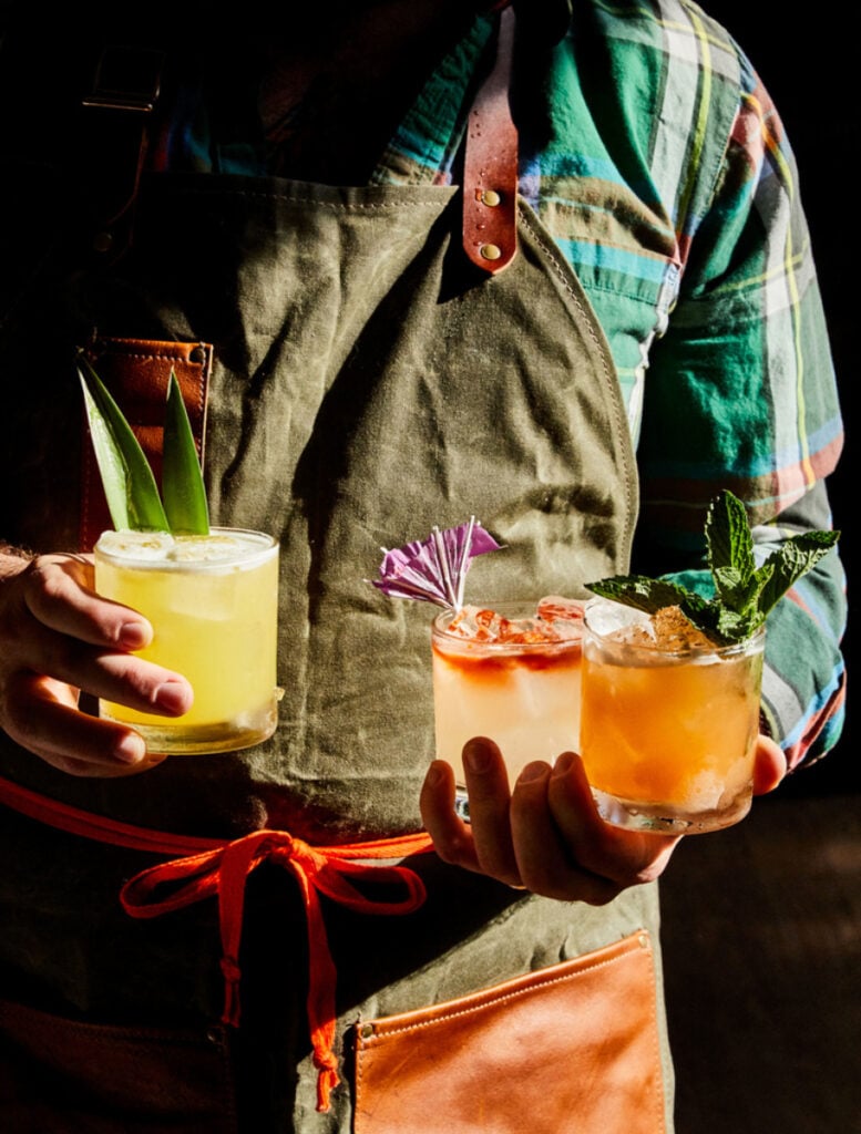 A bartender holding three colorful cocktails by Peter Frank Edwards of Charleston, South Carolina
