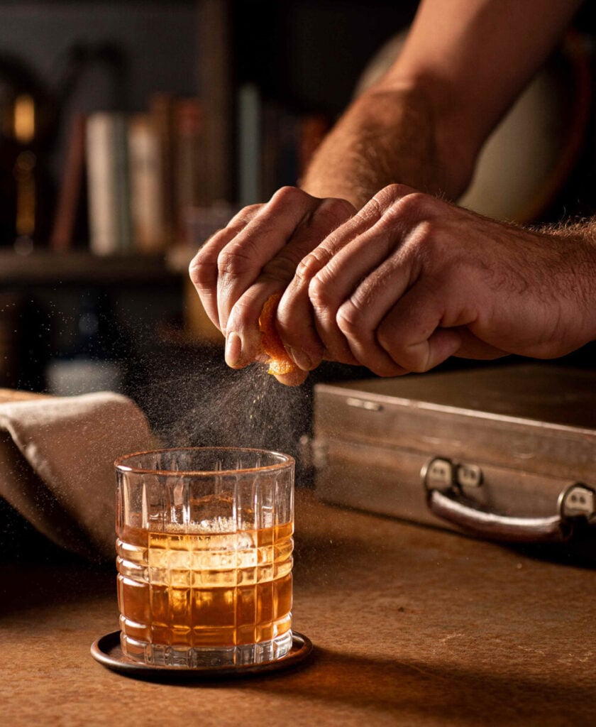 A bartender spritzing orange into a whiskey cocktail by Rebecca Peloquin