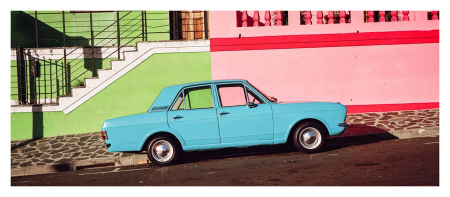 A vintage, baby blue Mercedes parked perfectly in the middle of two houses, one Cosmo Green and the other Wanda Pink by photographer Saam Gabbay of Venice, California