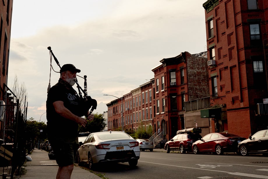 Lone bagpipe player on the sidewalk of a New York street, by Stephen Speranza