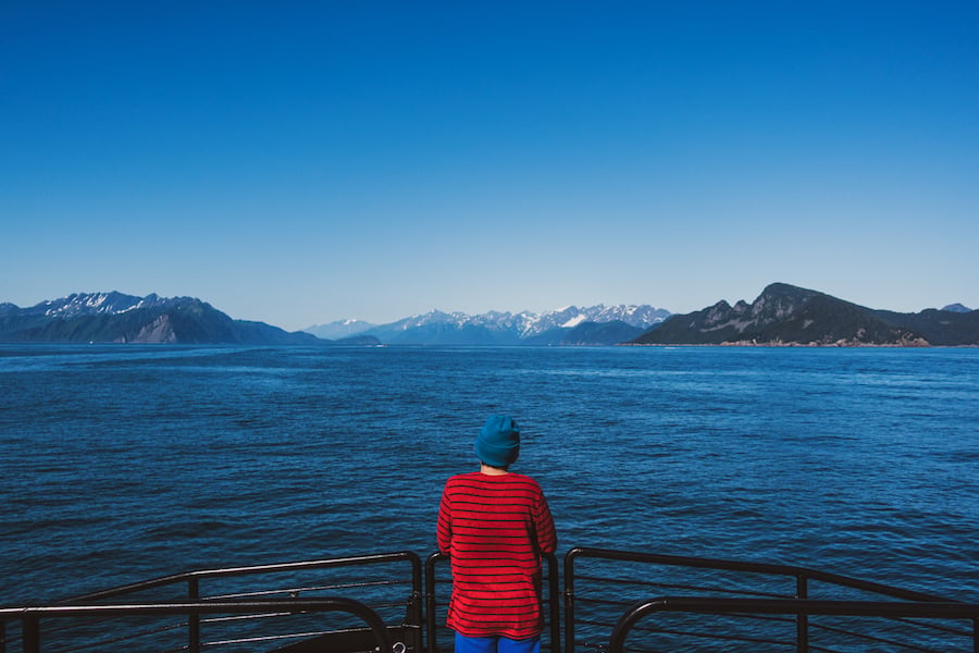 A man looks out into a bay with snow capped mountains in the distance by photographer Steve Boyle of Philadelphia, Pennslyvania. 