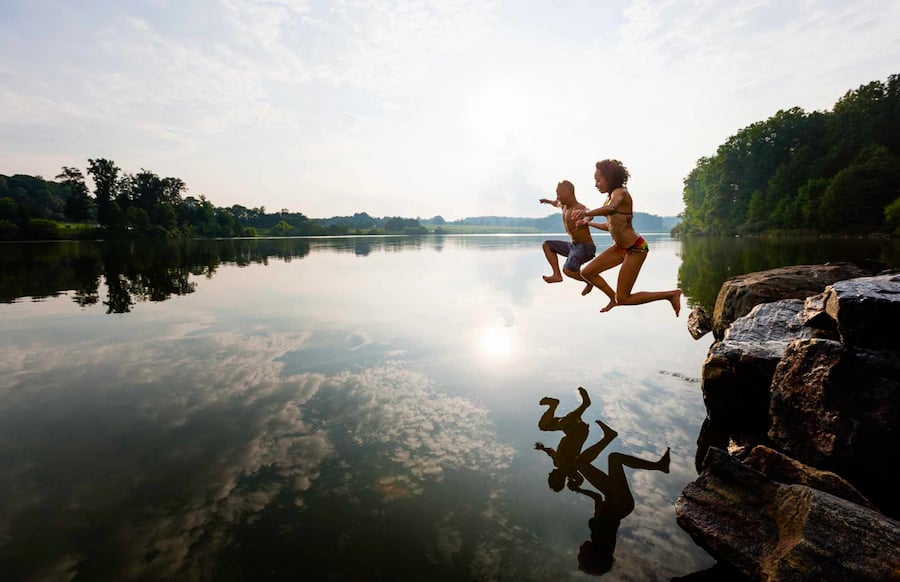 a couple jumping off a rock into a beautiful lake in Valley Forge National Park by photographer Zave Smith of Philadelphia, Pennsylvania. 