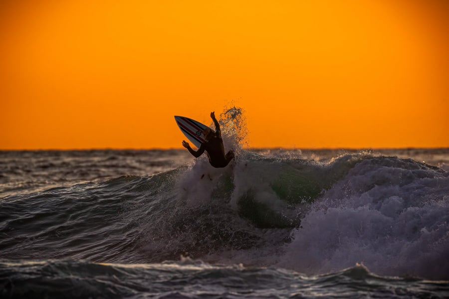 A surfer catches a buge wave in front of an orange sky by photographer Aaron Ingrao of Buffalo, New York.