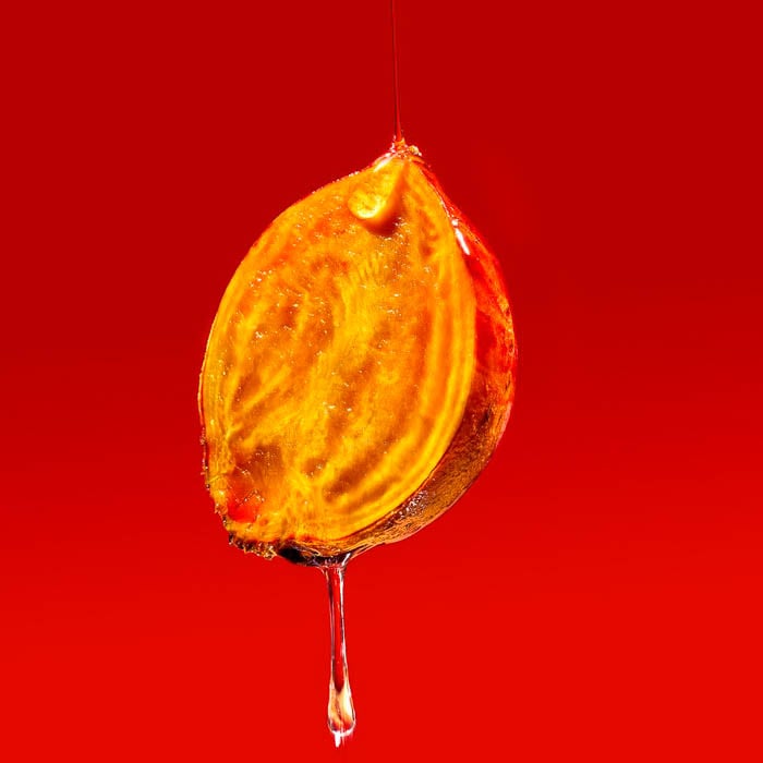Photo of syrup dripping down a sliced piece of fruit against a red background taken by New York-based food photographer Aaron Kyle Barton. 