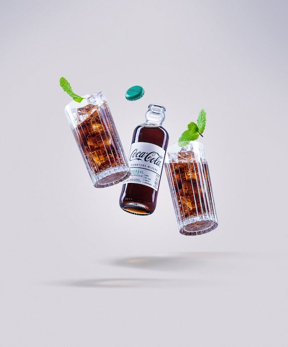 Image of suspended bottle of Coco Cola with two glasses and mint leaves, by London product photographer Andrew Currie.