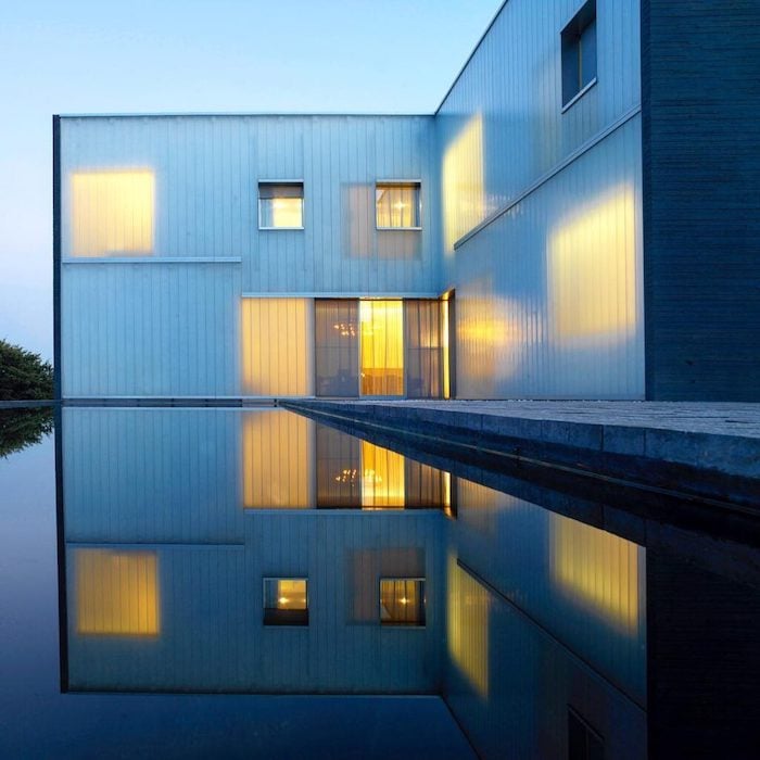 Photo by Andy Ryan of a rectangular house overlooking a reflecting pool that mirrors its exact image and dimensions. 