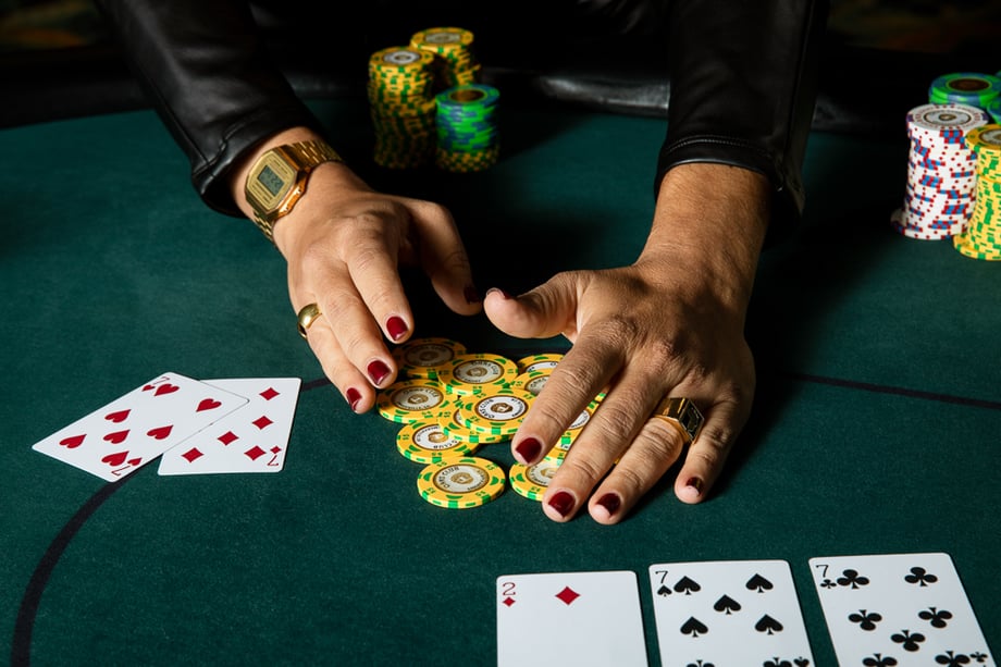 A woman's hands collecting yellow and green poker chips on a green felt table with cards lying around. 