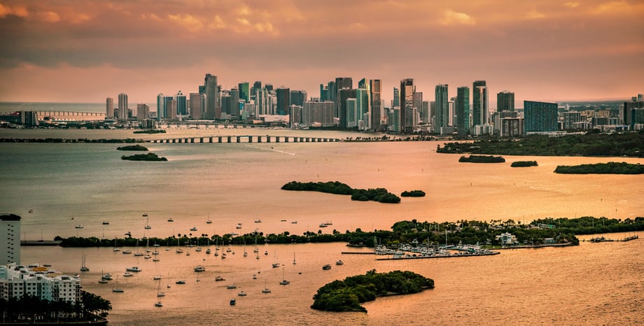 Aerial photo by Antonio Chagin of Miami at a distance over the water during sunset.