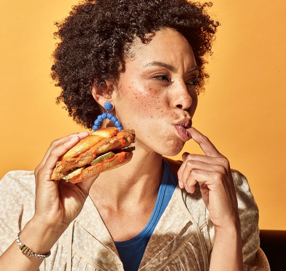 Photo of a woman licking her finger while eating a Zaxby's chicken sandwich taken by Black Horse Productions. Zaxby brand, axbys.com, friend chicken branding, fast food, chain restaurant, friend chicken chain, fried chicken restaurant, fried chicken photography, phoode, food photography production, food photography producer, food stylist, fried chicken food styling, fried chicken food photographer, fried chicken food photography