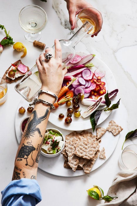 Photo of a woman's hand pouring a drink while a platter of veggies and pita sits beneath, taken by New York-based food photographer Bobbi Lin. 