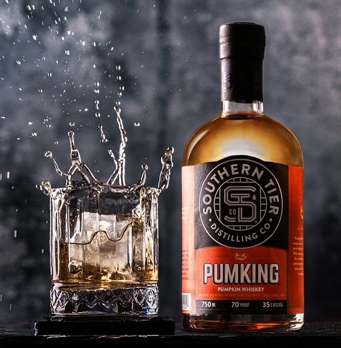 Icecubes make a splash in a glass of Southern Tier Distilling Company's Pumpkin Whiskey, photographed beside the bottle