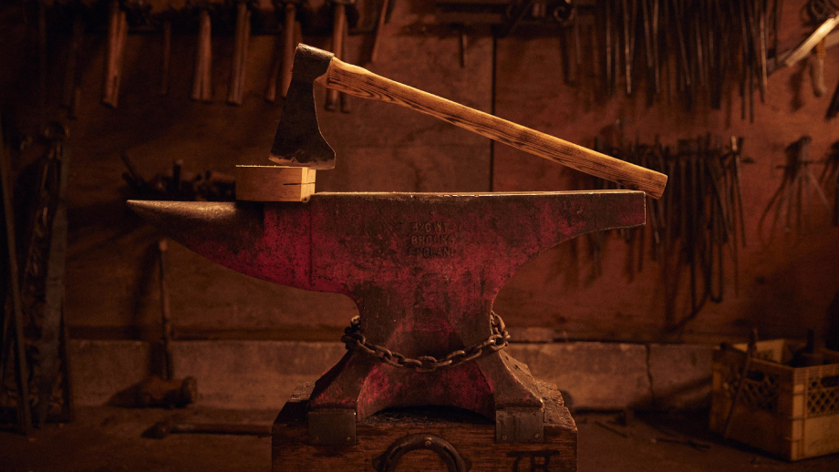 Photo of an axe laying on a block of wood and anvil taken by Christian Tisdale. 