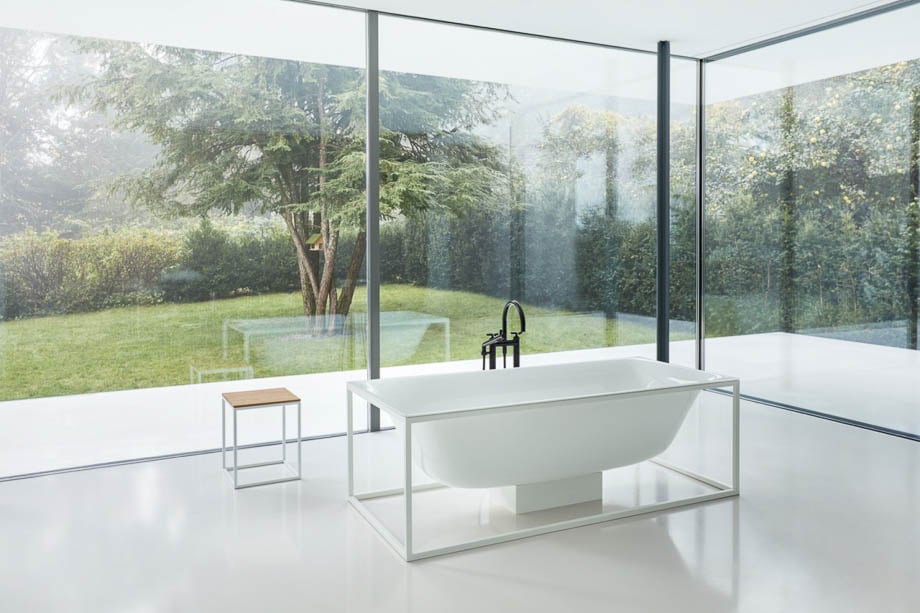 Photo of a white bathtub overlooking a garden through transparent glass walls taken by Berlin-based product photographer Christoph Sagel. 