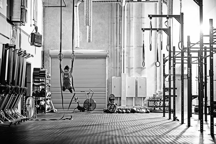 Black and white photo of a woman doing crossfit ring pull-ups taken by Christopher Robbins. 