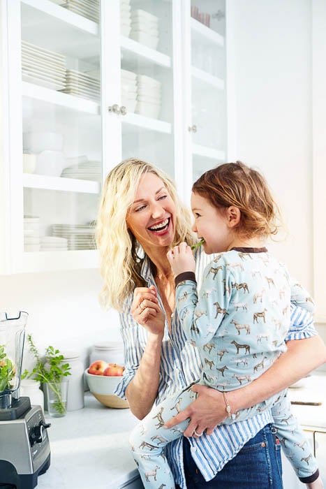 Photo of a mother holding her daughter in the kitchen while she eats some greens taken by San Francisco-based lifestyle photographer Colin Price. 