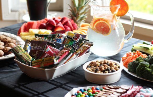A craft services table which includes water, snacks and healthy fruit options. 