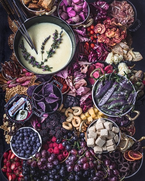 Colorful cheeseboard featuring Mifroma fondue surrounded by purple and pink fruits and vegetables and crackers and cookies, by Los Angeles product photographer Daniela Gerson,
