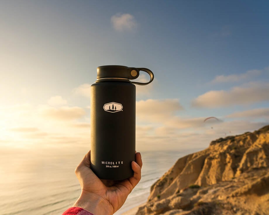 Photo of a man holding a black Microlite water bottle on a beach cliff  taken by Atlanta-based product photographer Daryl Spiegel. 