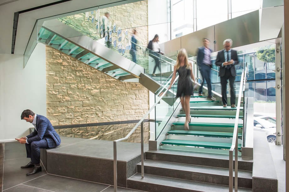 Photo of a man on his phone seated down at work while his co-workers speed by down a staircase taken by Los Angeles-based corporate photographer Ed Carreón. 