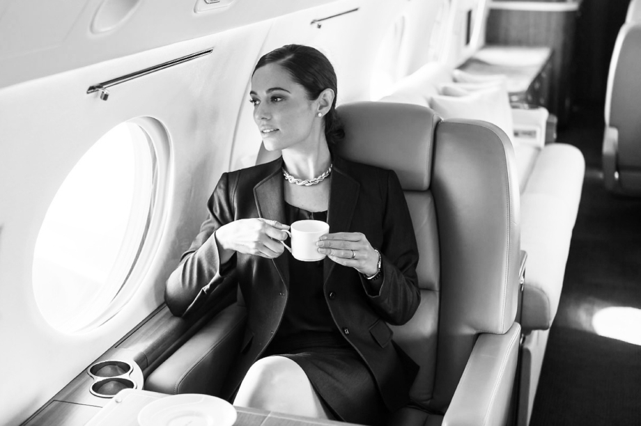 Black and white photo of a businesswoman drinking a cup of tea aboard a private jet. 