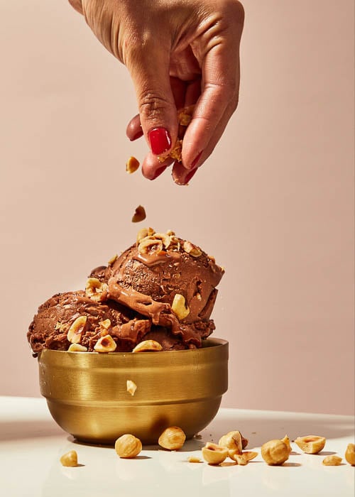Photo of a hand dropping cut pieces of nuts on top of chocolate ice cream taken by New York-based food photographer Evi Abeler. 