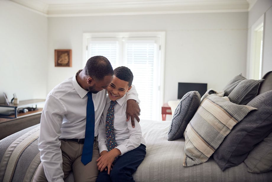 African American father talking with mixed-race son in bedroom.