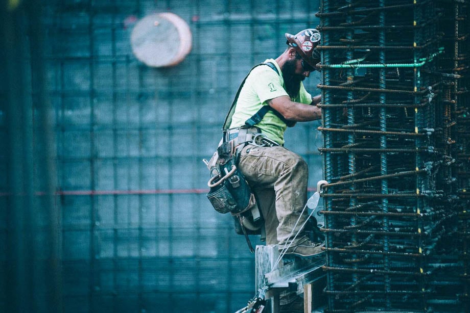Photo of a bearded construction worker climbing down a construction pillar taken by Los Angeles-based industrial photographer Gary Copeland. 