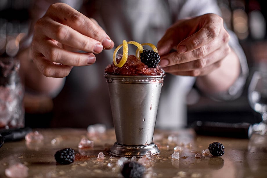 Portrait of bartender garnishing frozen cocktail with lemon peel and blackberries, by Atlanta food photographer Hiedi Harris.