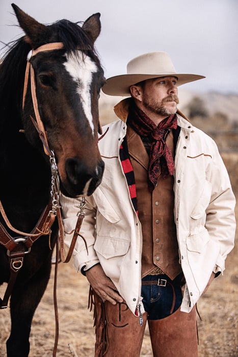 A cowboy standing next to his horse. 