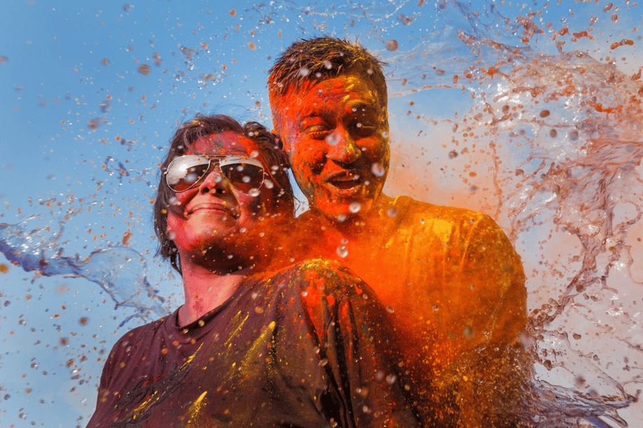 Picture of couple (one wearing sunglasses) experiencing colorful dust and liquid being thrown at them from all sides, by Mumbai-based portrait photographer Parikshit Rao.