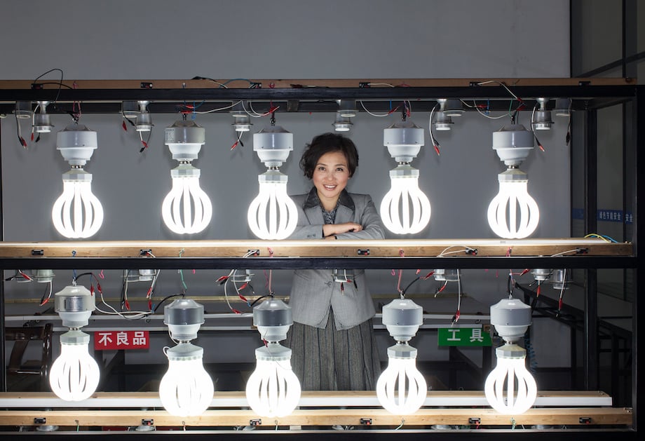 Portrait of figure smiling behind two rows of illuminated light bulbs, by Philadelphia corporate photographer James Wasserman.