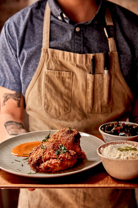 Photo of a chef holding a plate of food, including a fried piece of chicken, taken by Jason Varney. 