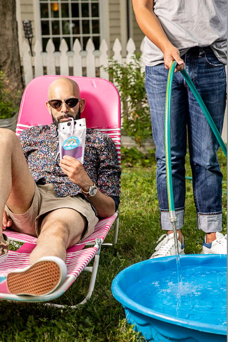 Photo of a man sipping a drink while reclining on a chair while a woman fills up a plastic bucket in the backyard taken by Washington DC-based lifestyle photographer Jennifer Chase. 