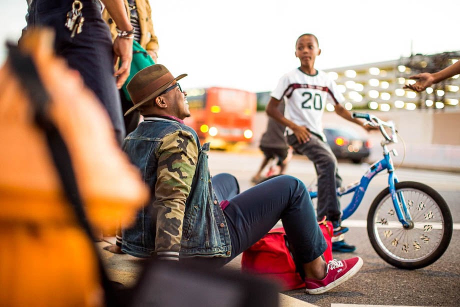 A photo of a group of people hanging out curbside, with a man laughing and a kid on a bike, taken by Los Angeles-based lifestyle photographer John Davis. 
