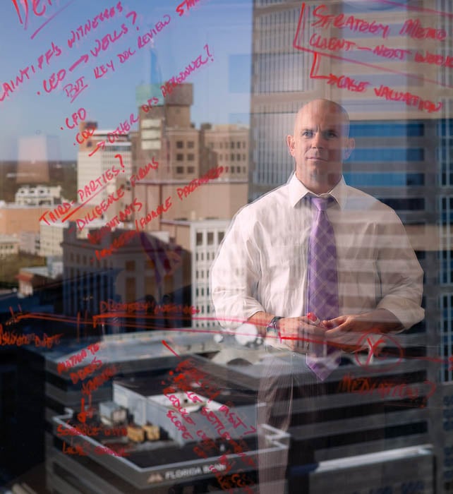 Photo of a bald businessman writing with a red marker on a glass wall taken by Miami-based corporate photographer John Lair. 