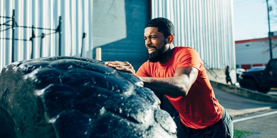 An African-American man doing a tire flip outside a gym taken by Chicago-based sports and fitness photographer Jon Hamblin. 