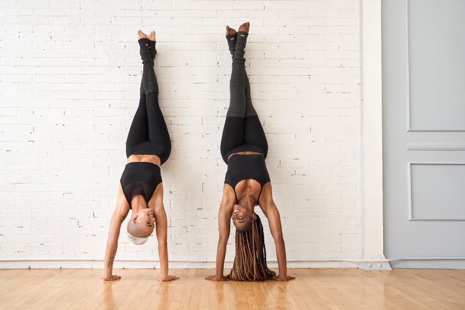 Photo by Justin L’Heureux of two women doing handstands in a yoga studio.