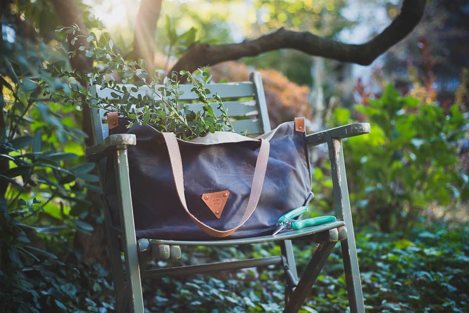 Photo of a navy blue gardener's bag outside resting on a wooden chair with leaves in it taken by Philadelphia-based product photographer Kira Luxon. 