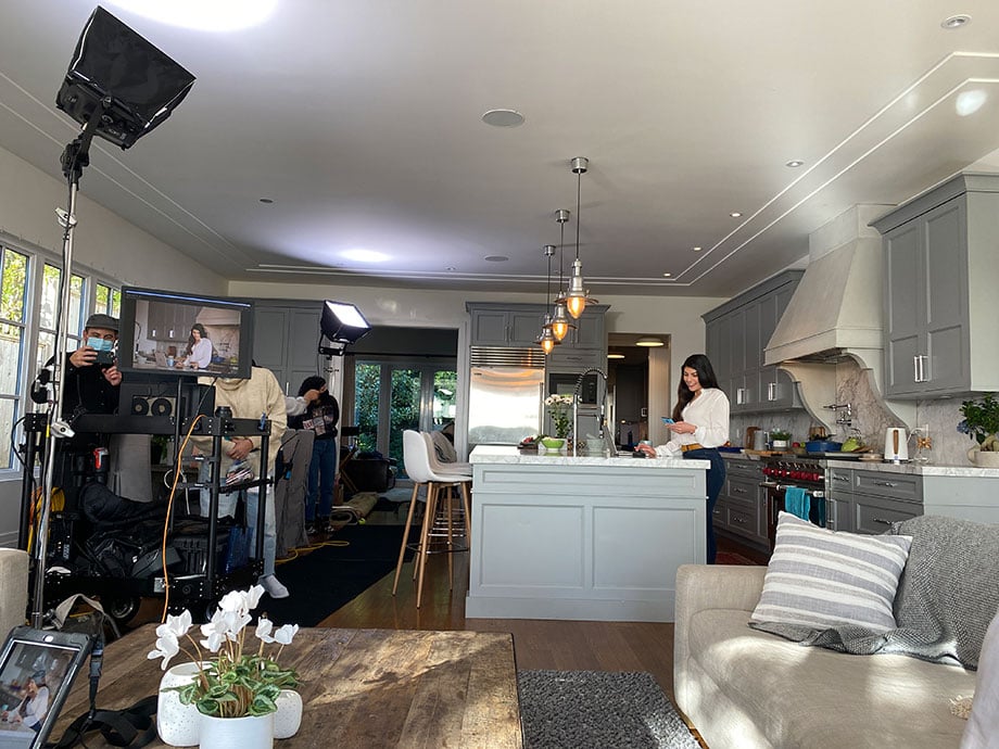 A behind the scenes image showing a monitor and equipment as a model poses in a well-lit kitchen