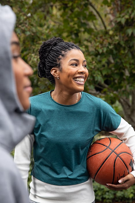 A basketball player smiling wide as she holds the ball in her arm, shot for Invisalign Global