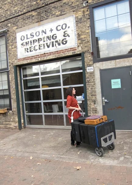 A woman stands outside a building with a dolly of photography portfolios 