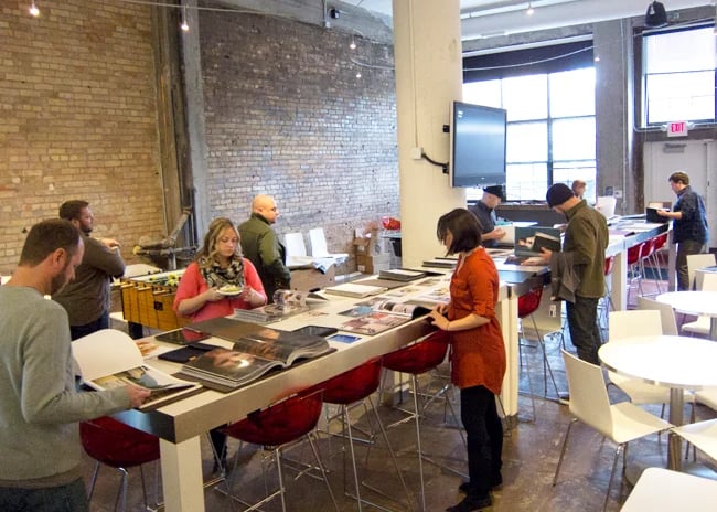 A team of creatives gather around a large white table covered with photography books