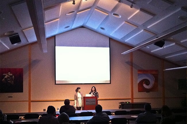 Two women at the front of a room giving a presentation in front of a large screen
