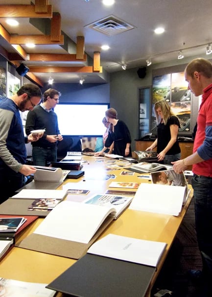 People flip through photo portfolios that are stretched across a long table