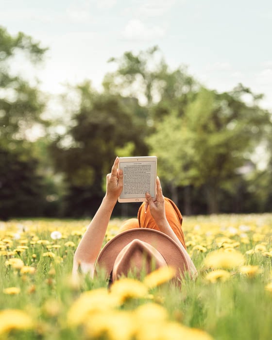 Photo of a woman reading on a tablet while lying down in a field of sunflowers taken by Toronto-based product photographer duo Raina Kirn and Wilson Barry of Rain+Wilson. 