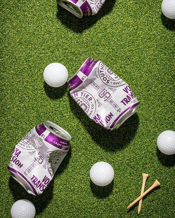 Crushed Vodka Transfusion cans from Southern Tier Distilling Company shown against a fake-grass background, alongside golf