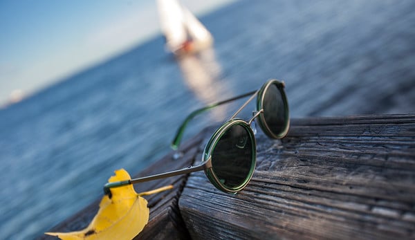 Photo of sunglasses resting on a wooden ledge overseeing the ocean taken by Miami-based product photographer Ricardo Cornejo. 
