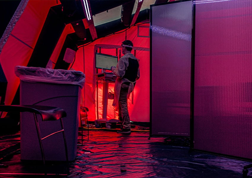 Ronnie Orlando's shot of a worker in PPE standing at a computer terminal in an isolation tent