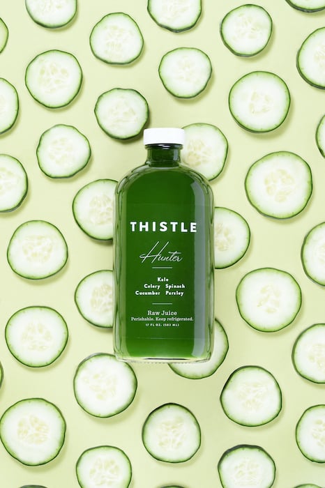 Product photo of green raw juice with sliced cucumber backdrop, by Los Angeles product photographer Sedona Tuberville